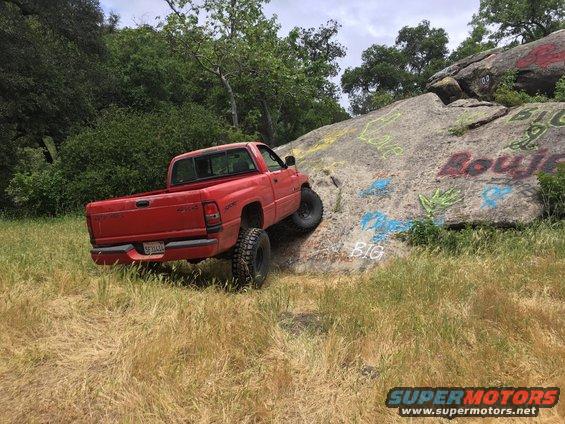 1996 Dodge 1500 pickup truck climbing a grassy, graffiti-covered rock face