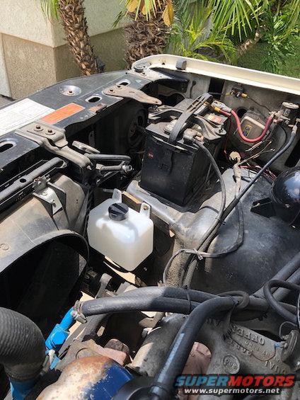 engine bay with battery, coolant reservoir, hoses, and some engine parts visible
