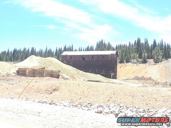 old wooden building next to large piles of material, trees in background