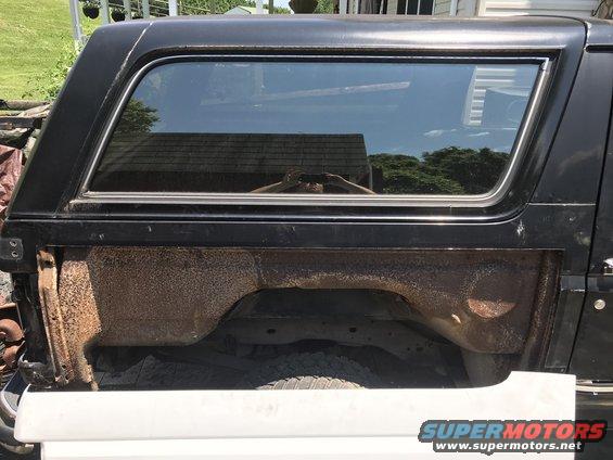 Side view of a black Ford Bronco with significant rust on the rear wheel well and lower body