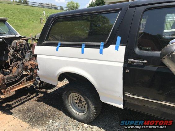 1992 Ford Bronco rear quarter panel, white, with blue tape, next to a disassembled vehicle