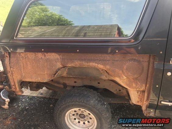 Black SUV's heavily rusted rear fender well and quarter panel, with a visible tire and suspension components