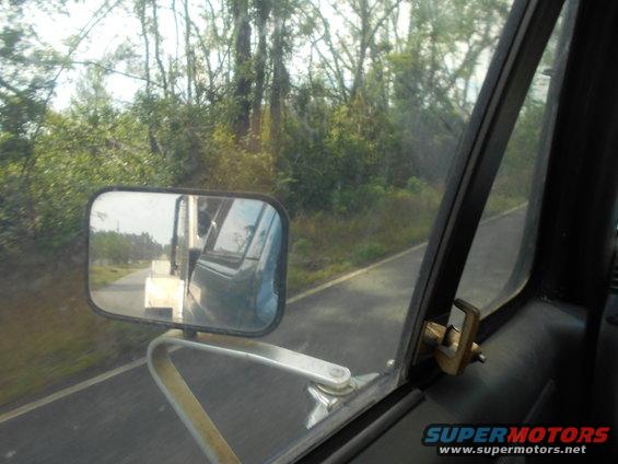 View from inside a vehicle, looking out the passenger side window and in the side mirror. Another vehicle is visible in the mirror
