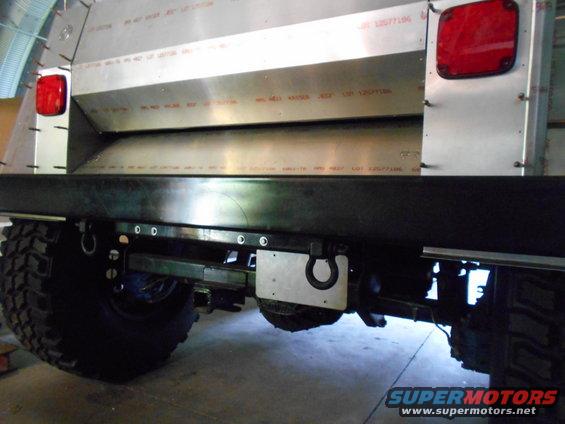 Rear view of a vehicle with large off-road tires, custom metal bodywork, and red taillights