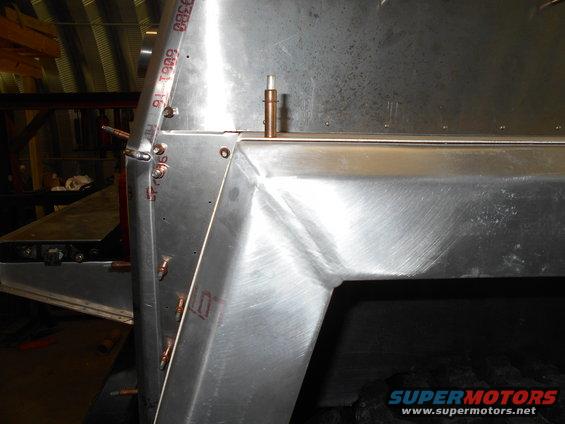 Metal frame section with rivets and copper fittings, showing brushed metal texture and some red markings