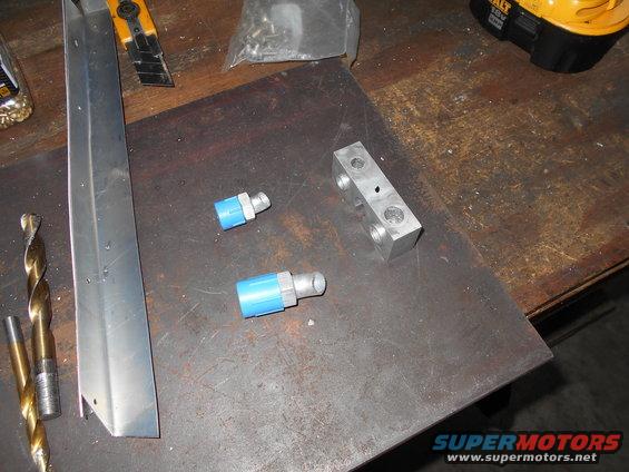 Two blue air fittings and a metal block sit on a workbench next to drill bits and a utility knife