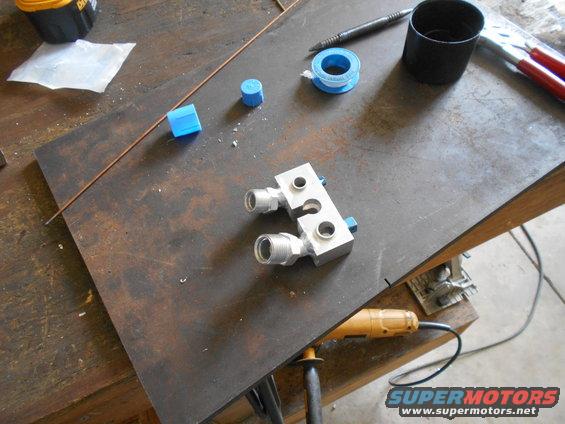 Metal manifold with threaded fittings and blue caps on a workbench with tools