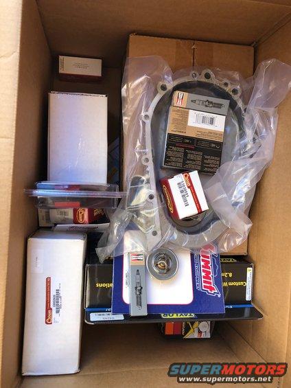 Box of engine parts including spark plugs, a thermostat, and a timing cover gasket