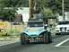 1970 Volkswagen Beetle - A light blue dune buggy with custom stripes and a roof-mounted cargo box drives down a paved road.