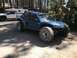 1970 Volkswagen Beetle - A custom blue buggy sits parked on a dirt road next to a white pickup truck with a camper shell, surrounded by trees.