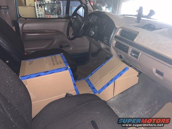 Interior of a green 1992 Ford F-150 XLT showing the dashboard, steering wheel, and seats with cardboard boxes