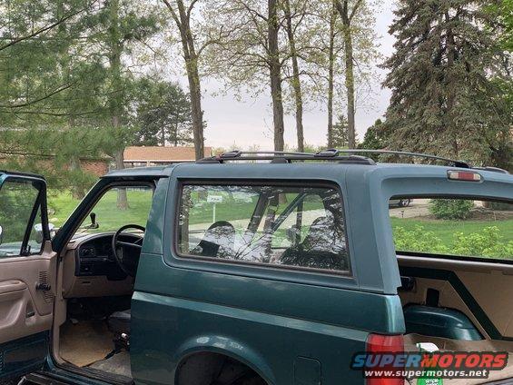 Green Ford Bronco side view, doors open, interior visible, roof rack, trees and houses in background