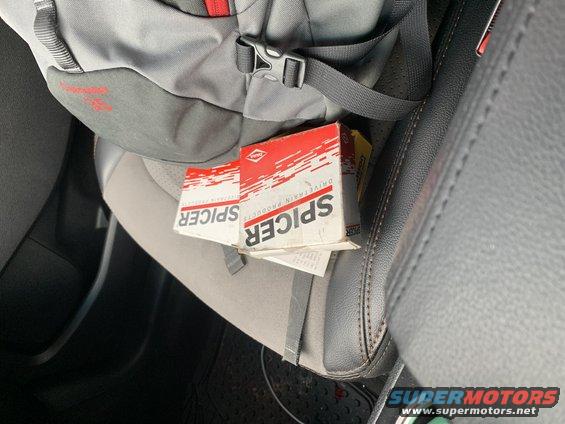 Two Spicer drivetrain parts boxes on a car seat next to a backpack