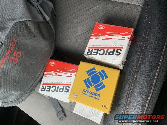 Three boxes of auto parts, including Spicer and Precision Universal Joint, sit on a car seat next to a backpack
