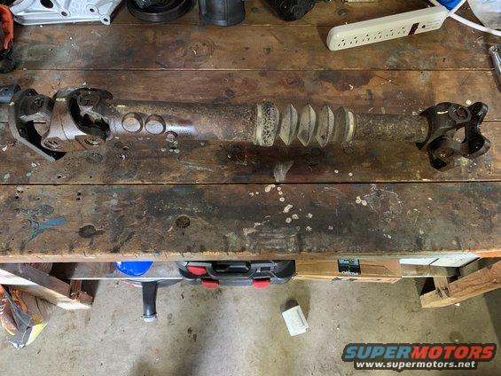 Driveshaft with U-joints and a rubber boot, resting on a wooden workbench
