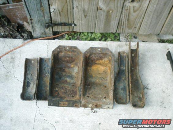 Several rusty metal brackets and plates laid out on concrete