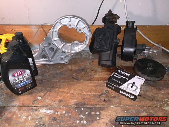 Automotive parts including a power steering pump, bracket, and pitman arm puller kit on a wooden surface