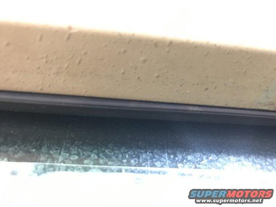 Close-up of a tan vehicle body panel above a window with water spots. Supermotors.net logo visible