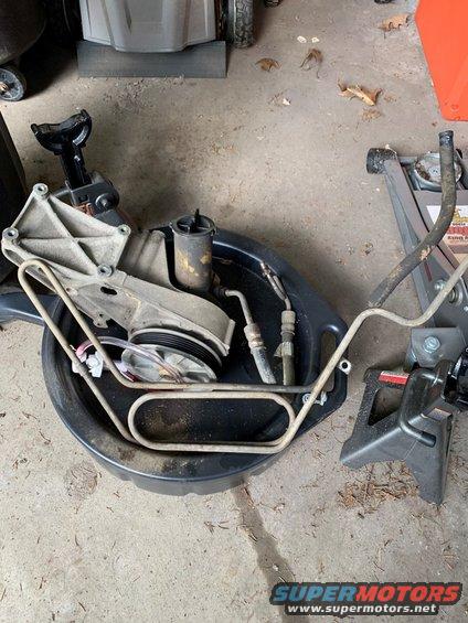 Power steering pump, pulley, and fluid lines in a drain pan with jack stands nearby
