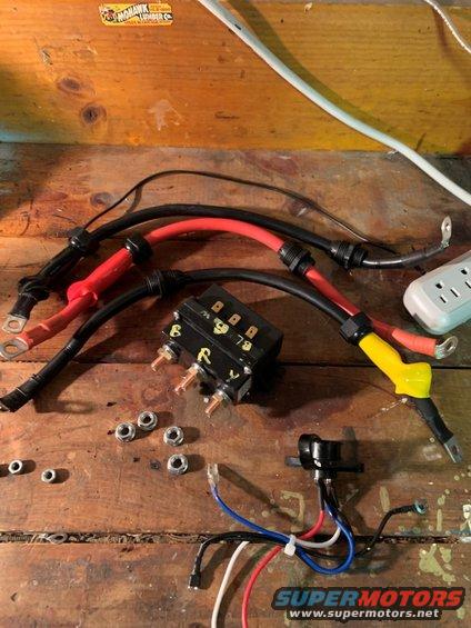 Automotive electrical components including a relay, heavy gauge wires, nuts, and a fuse holder on a wooden surface