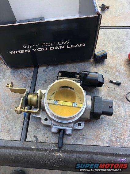 Throttle body assembly with attached sensor and linkage, next to an open box with text