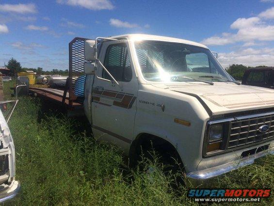 White Ford Econoline truck with a flatbed and cage in tall grass