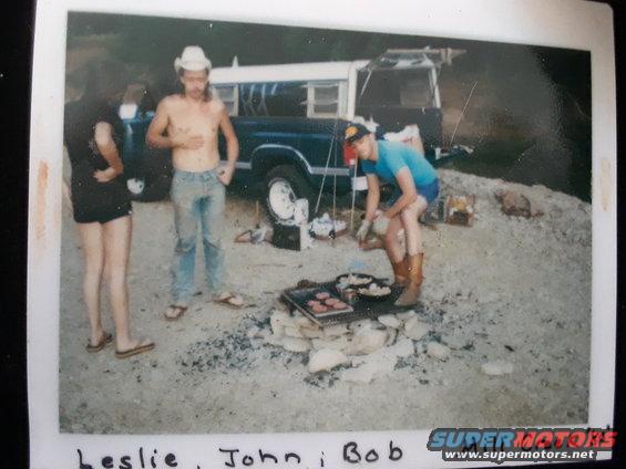 Dark blue Ford F-Series truck with white camper shell, side view, parked on gravel