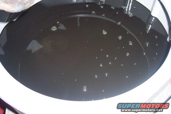 dirty oil with bubbles in a white pan, Supermotors.net logo at bottom right