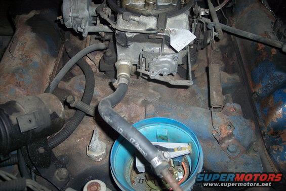 Engine bay with carburetor, distributor cap, and hoses. Blue paint on metal surfaces