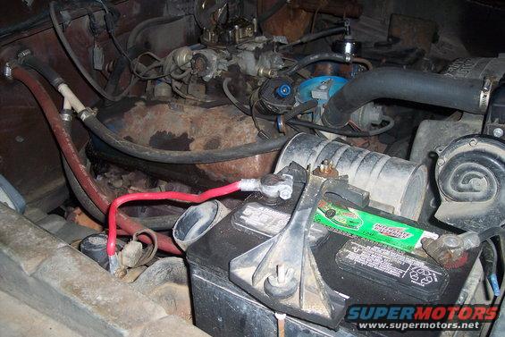 Engine bay with battery, hoses, and carburetor visible