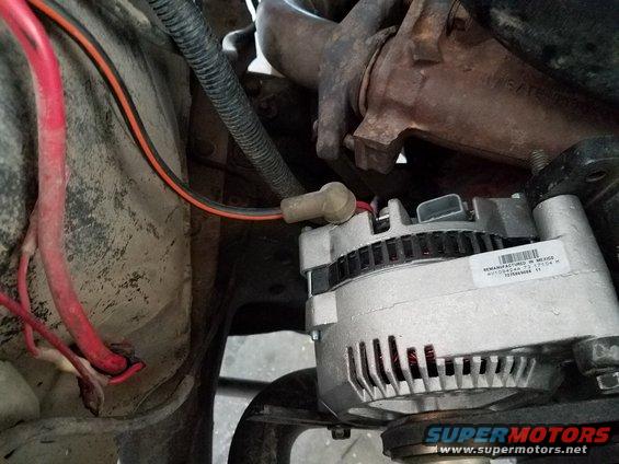 Remanufactured alternator with part number F1054AA 73 17104 M, mounted near engine components and wiring