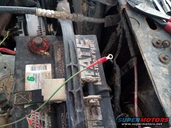 Car battery with red and green wires connected, pliers visible