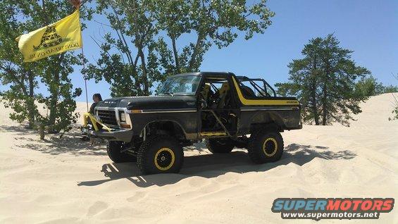 Modified 1978 Ford Bronco with roll cage and yellow accents on sand dunes