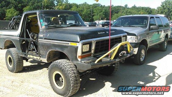 Black Bronco with roll cage and yellow seats next to a silver SUV