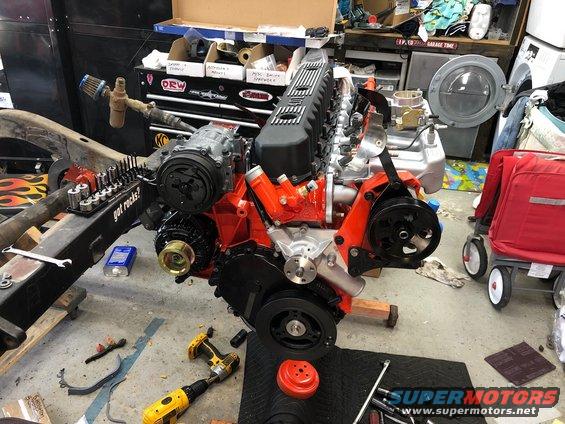 Engine assembly with orange block, black valve cover, and chrome accessories on a workshop floor