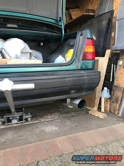 Green car rear with open trunk and chrome exhaust pipe