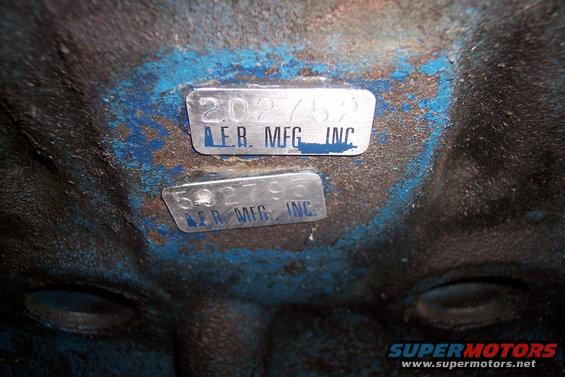 Two metal tags on a blue surface, one reads '202/52 AER. MFG. INC.' and the other '502795 AER MFG. INC.'