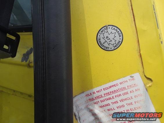 Yellow vehicle door jamb with a Transport Canada sticker and a warning label about ambulance preparation