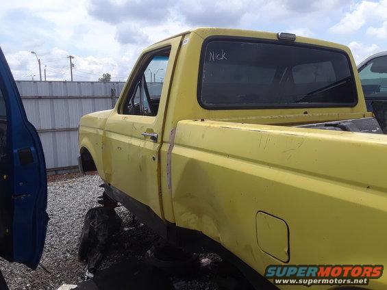 Yellow pickup truck, side view, with 'Nick' written on the rear window. Another vehicle's blue door is visible on the left