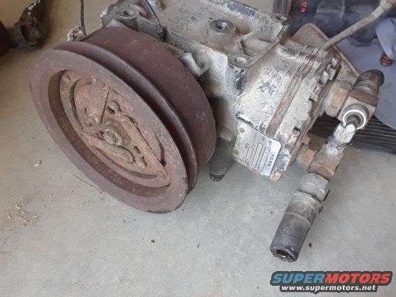 Old AC compressor with a rusty pulley and a metal tag that says YORK