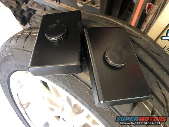 Two black rectangular suspension lift blocks with circular caps resting on a tire