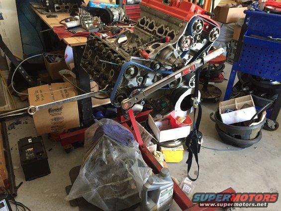 Engine on a red stand, with blue timing belts, in a cluttered garage