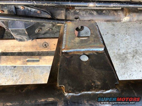 Welded metal bracket attached to a rusty vehicle frame, with a circular hole