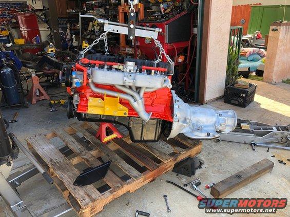 Engine and transmission assembly suspended by a hoist, resting on jack stands and a wooden pallet