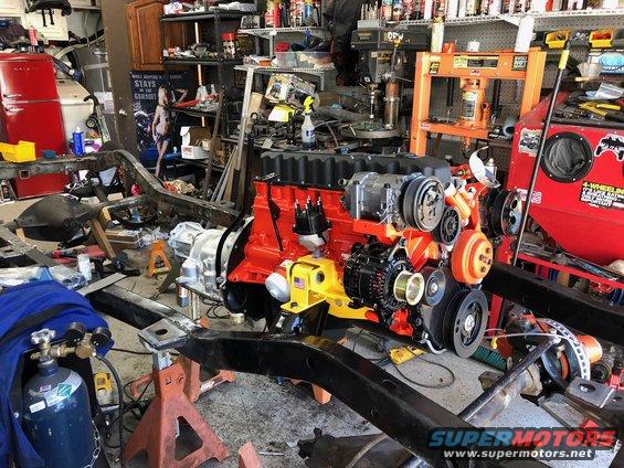 Rebuilt engine assembly with red block and orange accents, on stands in a cluttered garage