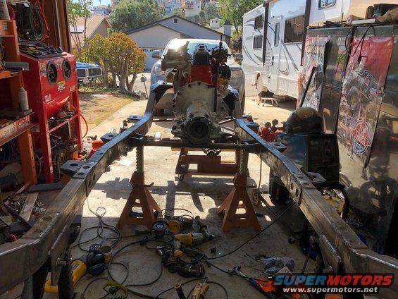 Vehicle frame on jack stands with engine in place. Tools and equipment are scattered around