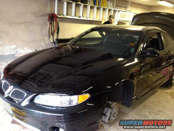Black 2000 Pontiac Grand Prix coupe, front wheels removed, hood open, parked indoors