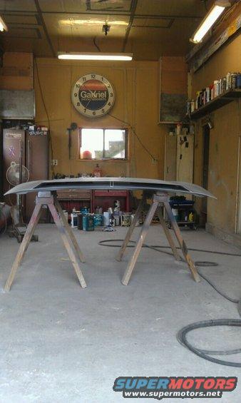 Car hood on sawhorses in a garage with a Gabriel clock on the wall