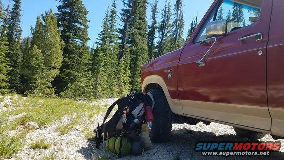 Red and tan Ford Bronco parked on a dirt road with camping backpacks next to it