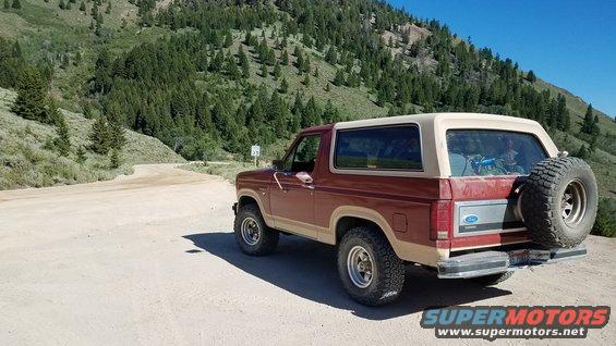 Ford Bronco parked on dirt road with mountains in background. Spare tire mounted on rear